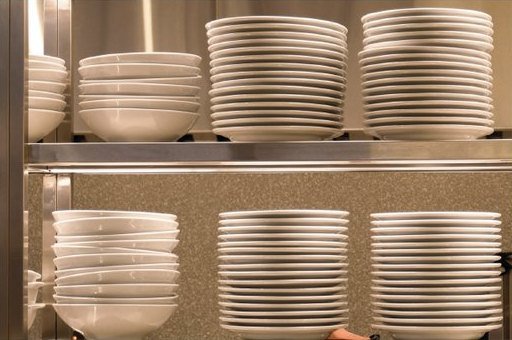 Pergamino: pilas de platos blancos ordenadas en una estantería.