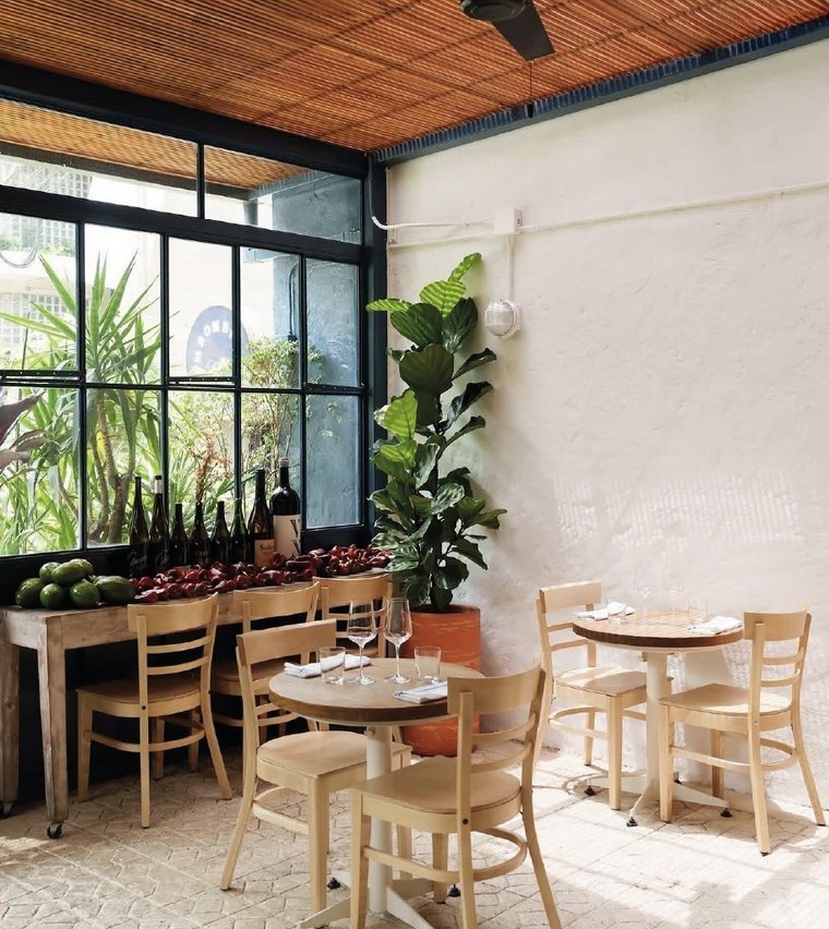 Sambombi: el comedor junto al ventanal, con sillas de madera y plantas.