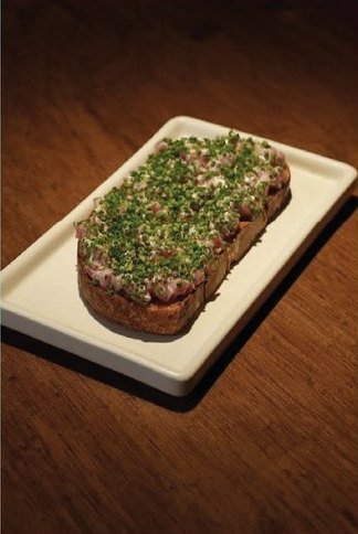 Sambombi: una tostada cubierta de hierbas picadas, servida sobre una tabla blanca.