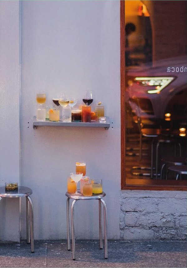 Susurro: la fachada al atardecer, con cocteles servidos sobre banquetas metálicas en la calle.