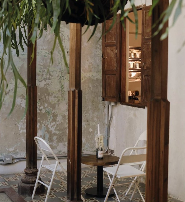 Persona Sala: el patio de la casa antigua, con columnas de madera, sillas blancas y plantas colgantes.