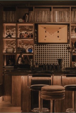 MALA: la barra, con estantes de madera llenos de botellas y una banqueta al frente.
