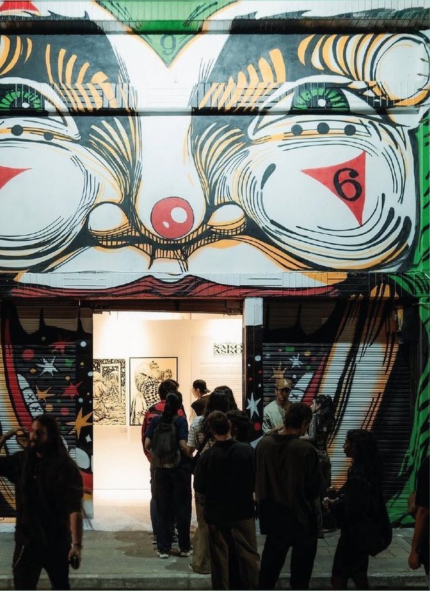 Base: la fachada de la galería, con un mural de dos ojos enormes sobre la entrada y gente entrando.